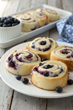 blueberry rolls on a white plate next to a bowl of blueberries