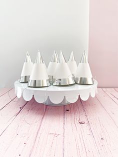 four white lamps sitting on top of a wooden table next to a pink painted wall