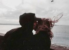 a man and woman sitting next to each other near the ocean on a cloudy day