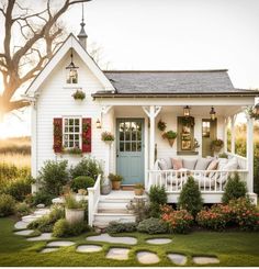 a small white house with red shutters and flowers on the front porch is shown