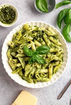 pasta with pesto sauce in a white bowl on a table next to cheese and basil leaves