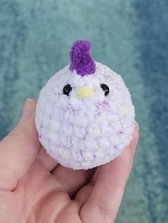 a hand is holding a small crocheted toy with a purple bird on it