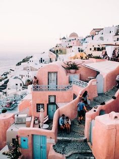 people are walking up the steps to some buildings on the cliff above the water in front of them