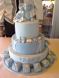 a baby shower cake with an elephant on top and letters around the bottom, sitting on a table in front of a woman