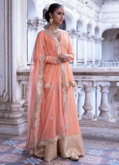 This look features a tangerine banarasi kurta sharara set. The georgette Benarasi kurta is a v neck, with full sleeves, empire cut and circular ghera. It is embellished with mirror, pearl and scallop gold laces. Teamed with a matching sharara with broad gold embroidery border. A matching net dupatta with a scallop border and bootis completes the look. Composition: Kurta - Viscose georgette Sharara-Viscose georgette Dupatta - Soft net Care: Dry Clean Only and Vacuum Storage This product can be customised for colour, sleeves, length of blouse and neck design Delivery : 2 weeks as the product is hand crafted. For more information and sizes please contact fabiliciousfashion@gmail.com or visit our Copenhagen studio. About the Designer : Renee Label was created in 2013,by the talented sister duo Festive V-neck Salwar Kameez For Wedding, V-neck Salwar Kameez With Dabka Work For Wedding, Festive V-neck Salwar Kameez With Zari Work, V-neck Salwar Kameez For Diwali Wedding, Wedding Salwar Kameez Semi-stitched V-neck, Semi-stitched V-neck Salwar Kameez For Wedding, Diwali V-neck Sharara With Dupatta, V-neck Salwar Kameez For Wedding And Diwali, V-neck Salwar Kameez For Wedding And Eid