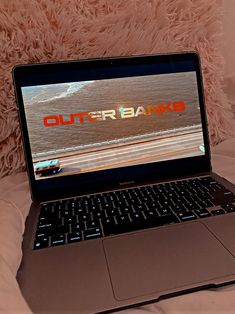 an open laptop computer sitting on top of a bed next to a fluffy pink pillow