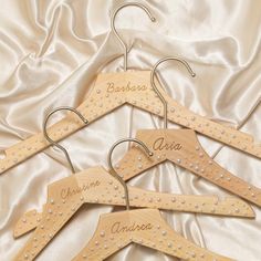 four wooden clothes hangers with personalized names on them, sitting on a white satin background