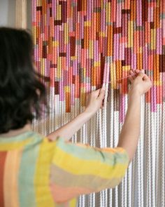 a woman is working on a wall hanging made out of strips of colored paper and yarn