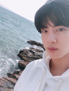 a young man standing on top of a rocky beach next to the ocean and looking at the camera