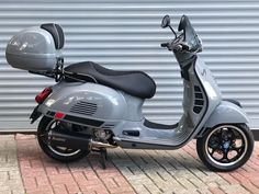 a grey scooter parked on the side of a brick road next to a garage door