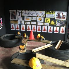 construction site with toy trucks, cones and construction signs on the wall behind them in front of children's play area