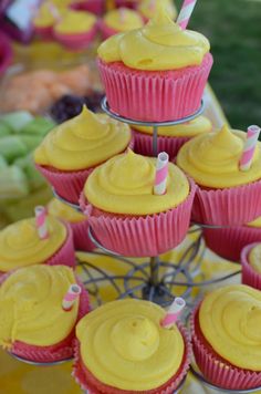 cupcakes with yellow frosting and pink icing are arranged on a table