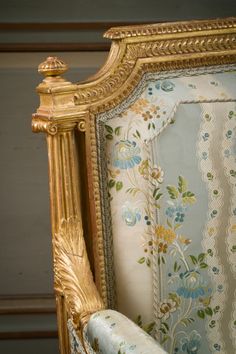 an ornate gold frame with blue and yellow flowers on it's back end, sitting in front of a striped wall