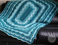 a blue crocheted afghan sitting on top of a black leather couch next to a pillow