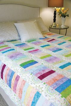 a bed with a multicolored quilt on it in a bedroom next to a lamp