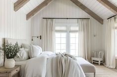 a bedroom with white bedding and wooden beams on the ceiling is decorated in neutral tones