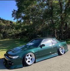 the green car is parked on the side of the road in front of some trees