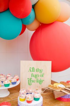 a table topped with lots of cupcakes next to balloons