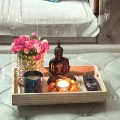 a tray with a buddha statue on top of it next to flowers and a remote control