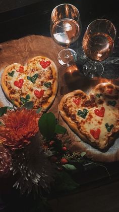 two heart shaped pizzas sitting on top of a table next to wine glasses and flowers