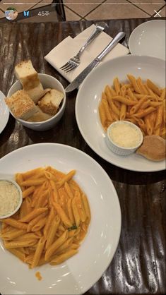 two white plates topped with french fries next to bowls of dip and bread on top of a wooden table