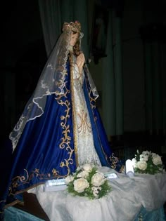 a statue of a woman dressed in blue and gold with flowers on the table next to it