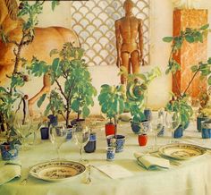 the table is set with plates, cups and vases filled with plants on it