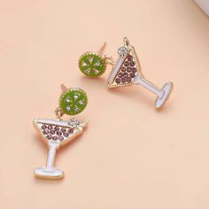 two different colored earrings on top of each other, one with a martini glass and the other with a slice of lime