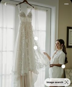 a woman standing next to a dress hanging on a window sill