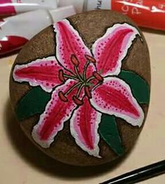 a pink flower painted on a rock next to some markers and paintbrushes in front of it