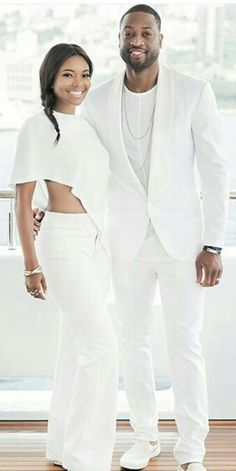 a man and woman standing next to each other in front of a white wall with windows