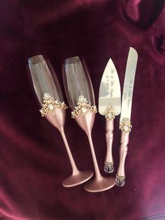 three wine glasses and a knife are sitting on a purple velvet surface, one is decorated with gold flowers