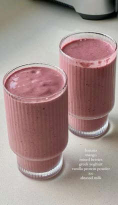 two glasses filled with pink smoothie sitting on top of a counter