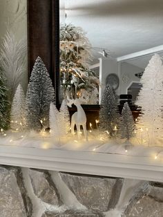 a fireplace mantel decorated with white christmas trees and fake reindeer figurines in front of a mirror