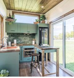 a kitchen with green cabinets and wooden flooring next to an open door that leads out onto a grassy field