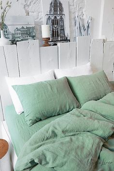 an unmade bed with green linens and white sheets in front of a wooden headboard