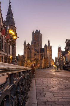 an old european city street at dusk with the sun going down on it's steeples