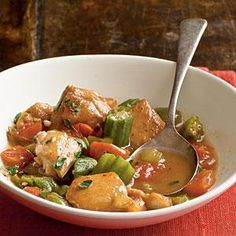 a white bowl filled with meat and vegetables on top of a red place mat next to a wooden table