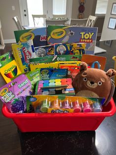 a red basket filled with lots of toys on top of a black table next to a brown teddy bear