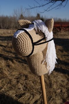 a crocheted horse head on top of a wooden stick in the middle of a field