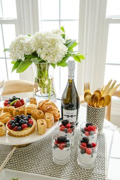 a table topped with desserts next to a bottle of wine and two vases filled with flowers