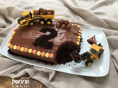 a birthday cake with chocolate frosting and construction trucks on top, sitting on a plate