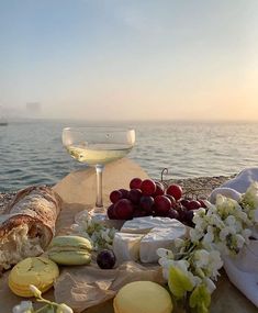 a table topped with cheese and fruit next to a wine glass filled with white wine