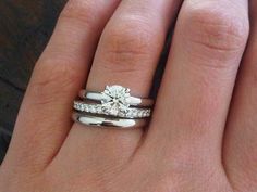 a woman's hand with two wedding rings on top of her finger and the ring has a diamond in it