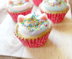 some cupcakes with white frosting and sprinkles on them sitting on a table