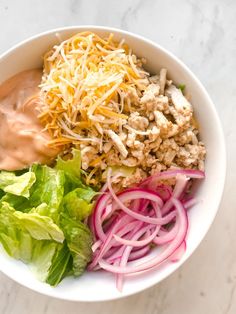 a white bowl filled with lettuce, meat and cheese on top of it