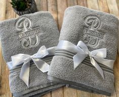 two gray towels with white bows and monogrammed lettering are on a wooden table