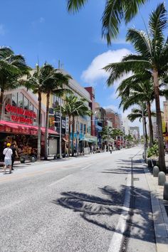 a man riding a skateboard down a street next to tall buildings and palm trees