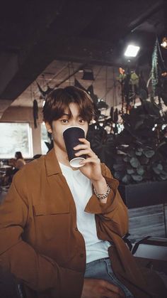 a young man holding a coffee cup in his right hand and looking at the camera