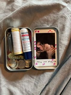 an open tin with some items in it on top of a bed next to a pair of scissors